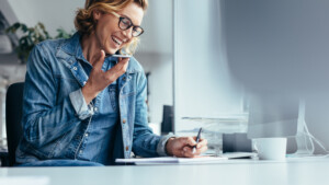 Eine Mitarbeiterin führt ein Telefonat und macht dabei Notizen – ein Moment konzentrierter Kommunikation im modernen Büroalltag
